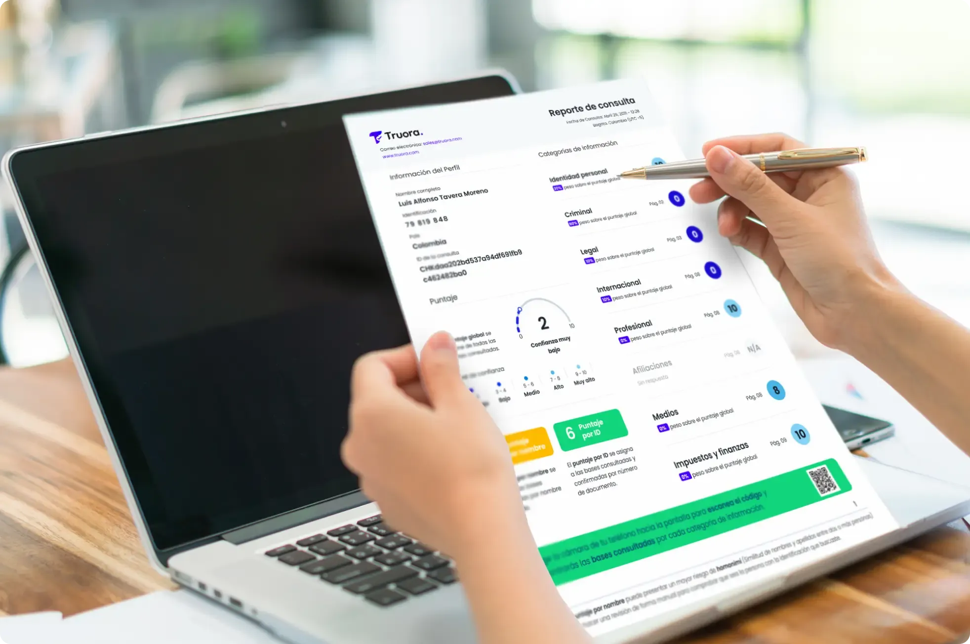 Hands holding a laptop showing the redesigned Truora background check report with categories and scores